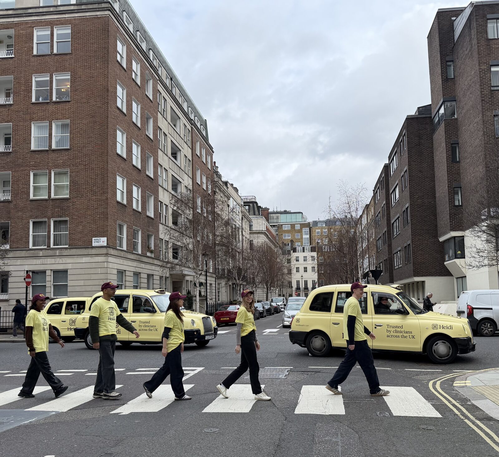 Heidi Health team in branded t-shirts crossing a zebra crossing on Harley Street next to a branded taxi