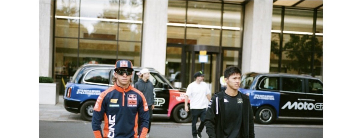 A fleet of branded MotoGP taxis lined up outside a venue with riders walking past